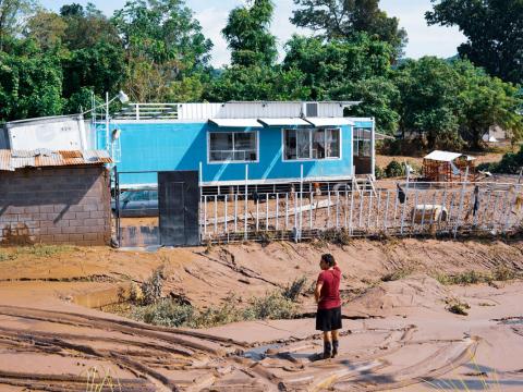 woman stands in front of home destroyed by hurricane in Honduras